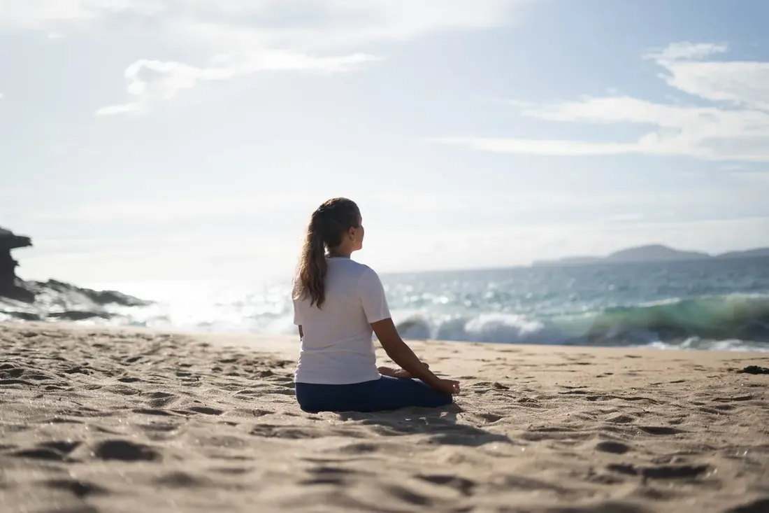 Mulher meditando na praia, de frente para o mar